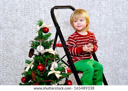 Adorable kid sitting on a ladder by the Christmas tree