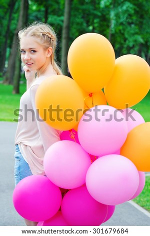 Portrait of beautiful teenager model walking with bright and colorful balloons in the park