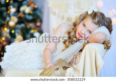 Christmas time, adorable girl in fancy dress sitting by the decorated Christmas tree