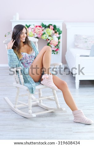 Beautiful woman dressed in fancy knitted clothes relaxing in white rocking chair in bedroom
