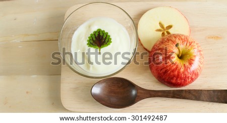 Natural low-fat yogurt with apple slice in the glass cup on wooden table.