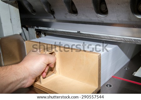 Front view of a paper guillotine used in commercial printing industry. Industrial knife cutter. Man\'s hand pushes the paper with special paper pusher