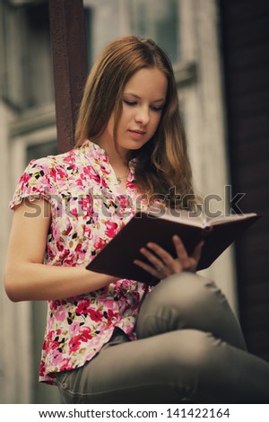 beautiful girl reading book sitting on the porch of  house