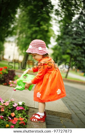 Cute curly girl watering flowers in the garden