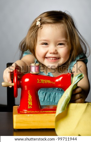 Cute little girl is playing with sewing machine