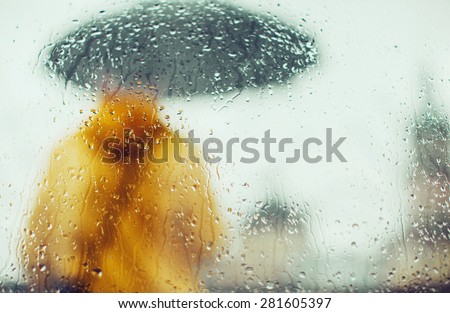 Man in yellow jacket with umbrella through glass with drops of water, on a background of city, rear view