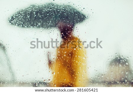 Man in yellow jacket with umbrella through glass with drops of water, on a background of city