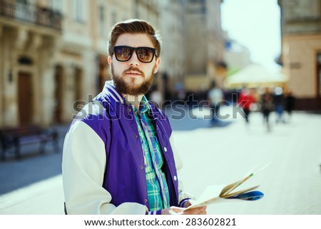 Stylish young bearded guy with map looking to the side on the streets of old European city
