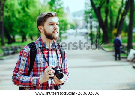 Young man with a beard holding old film camera and looking to the side, outdoors in the alley, in the park, profile