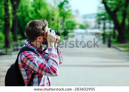 Young man taking photos on old film camera outdoors in the alley, in the park, profile