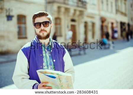 Stylish young bearded guy with map looking at camera on the streets of old European city