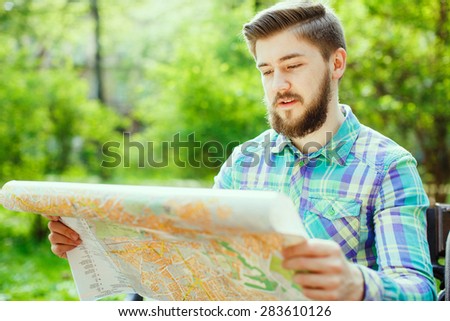 A young tourist with a beard smiling and sitting on a bench in the park, looking at the map, close-up