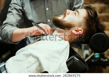 Barber shaving a bearded man in a barber shop, close-up