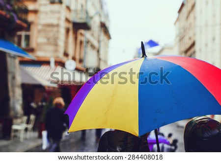 Colorful umbrella in the old city in a rainy day, soft-focus, rear view. Incidental people