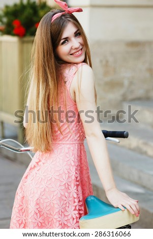 Young pretty blond-brown girl smiling in an old European city with vintage bicycle, looking at camera