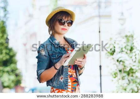 Young pretty woman tourist using tablet travel app guidebook in the old European city. Hipster style glasses and hat.