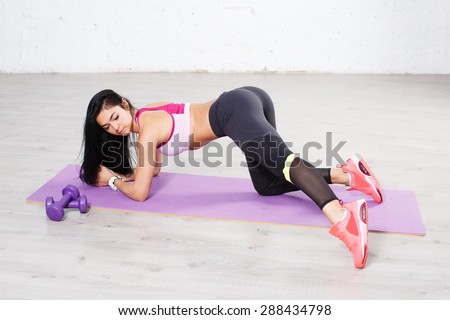 Pretty girl athlete with perfect body doing physical exercises for legs on yoga mat.