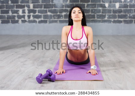 Sporty brunette girl doing exercises for flexible spine on brick wall background, yoga asana from Surya Namaskar sequence, Sun Salutation complex, urdhva mukha shvanasana (upward facing dog pose)