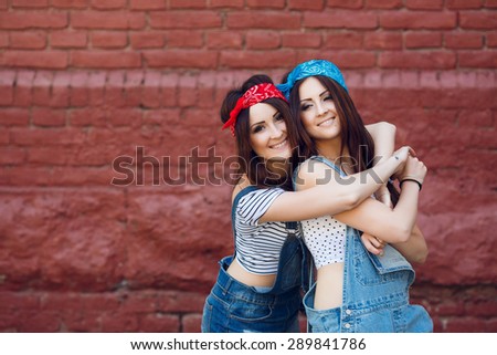 Happy twins girls, wearing bright bandanas, having great time together. Brick urban wall background.