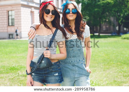 Portrait of two happy twins sisters stay together, wearing bright bandanas and stylish mirrored sunglasses, best fiend enjoy amazing time together.