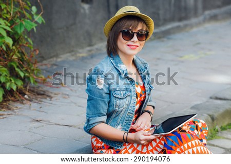 Close up smiling woman tourist sitting on the curb with tablet. In European city. Looking at the camera