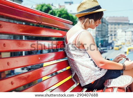 City stylish hipster tourist young woman, sitting on a red bench, using digital tablet.