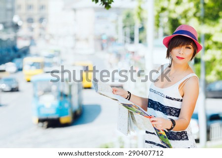 Cute tourist young woman with map. On city background. With shortcut dark-blonde hair. Wearing stylish pink hat, stripe white top.