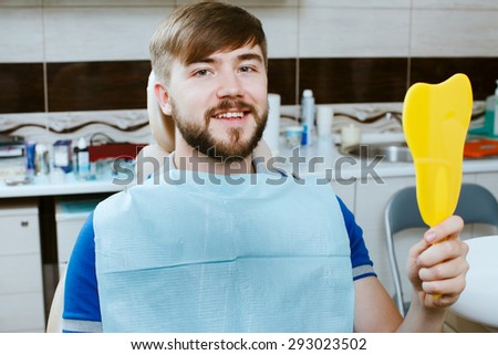 Smiling young man with mirror in the dentists chair.