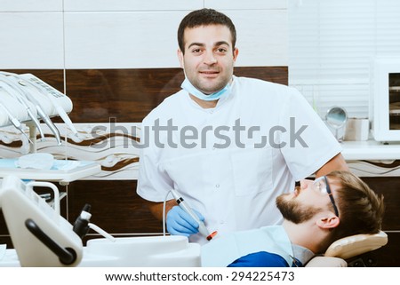 Male dentist with photopolymer lamp and male patient in dentist chair.