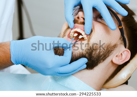 Select and check the color of the teeth in the dentist chair. Dentist makes the process of treatment of handsome young man.