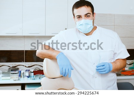 Dentist in medical mask leaning against dentists chair in dental clinic