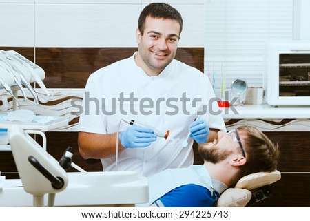 Happy dentist with photopolymer lamp and male patient in dentist chair.