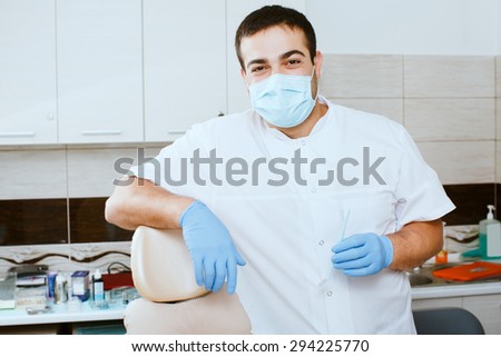 Male dentist in medical mask leaning against dentists chair in dental clinic