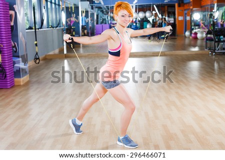 Young happy redhead  woman in sportswear doing exercises with fitness expander near the mirror in gym
