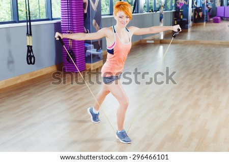 Young redhead  woman in sportswear doing exercises with fitness expander near the mirror in gym