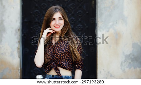 Smiling young woman wearing on dark blouse with long straight fair hair is looking at the camera on the street of old European city