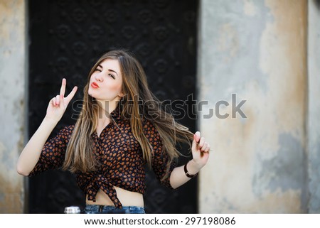 Positive cute girl with long straight fair hair wearing on dark blouse is posing on the bicycle on the street of old European city