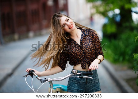 Pretty young girl with long fair hair wearing on blouse and shorts with bicycle having fun on the street