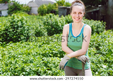 Young beautiful woman in working clothes and gloves, standing in the garden with instrument.