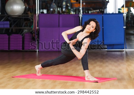 Positive fitness woman with curly hair wearing on black shirt and leggings posing in yoga asana on pink rubber mat at the gym