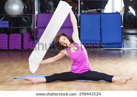 Athletic woman with dark hair wearing on violet shirt and black leggings does exercises on a yoga mate with a white core band on a sports equipment background at the gym