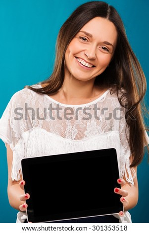 Pretty smiling girl, with long hair, wearing in white blouse, is posing with tablet, on blue background, waist up