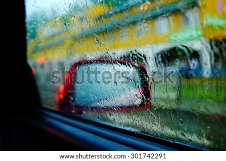 Beautiful abstract image of rain drops on a red car side view mirror and window, with street on a background, close up