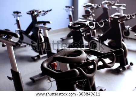 A lot of black exercise bikes in a bright gym room, with blue wall on the background, close up