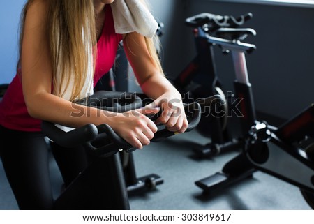 Cropped image of brunette girl with long hair, in sportswear, training on exercise bike in gym