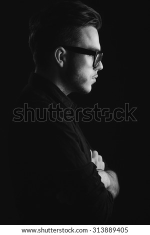 Side view of attractive young man wearing on the black shirt and glasses, on dark studio background, close up