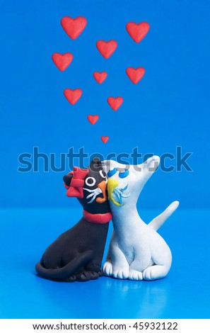 Two sweet clay black and white cats in love with each other. Blue copyspace for greeting text