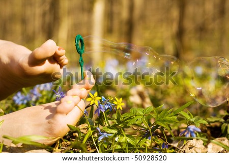 Barefooted tender woman\'s feet blow soap bubbles in spring flowers