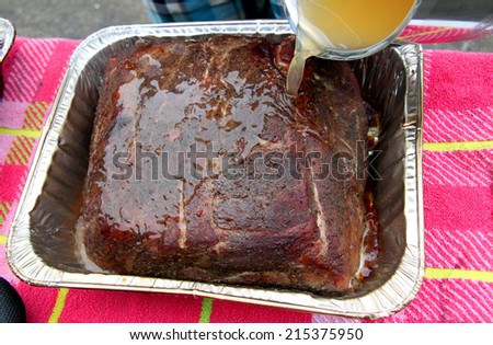 pouring juice and sauce over a smoked cooked pork roast in a pan