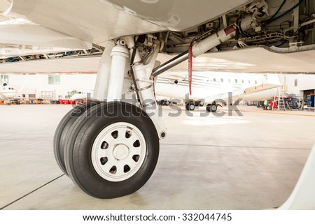 Detail of the wheel and landing gear on a small corporate passenger jet parked inside a hangar at an airport with a view of a second aircraft visible behind